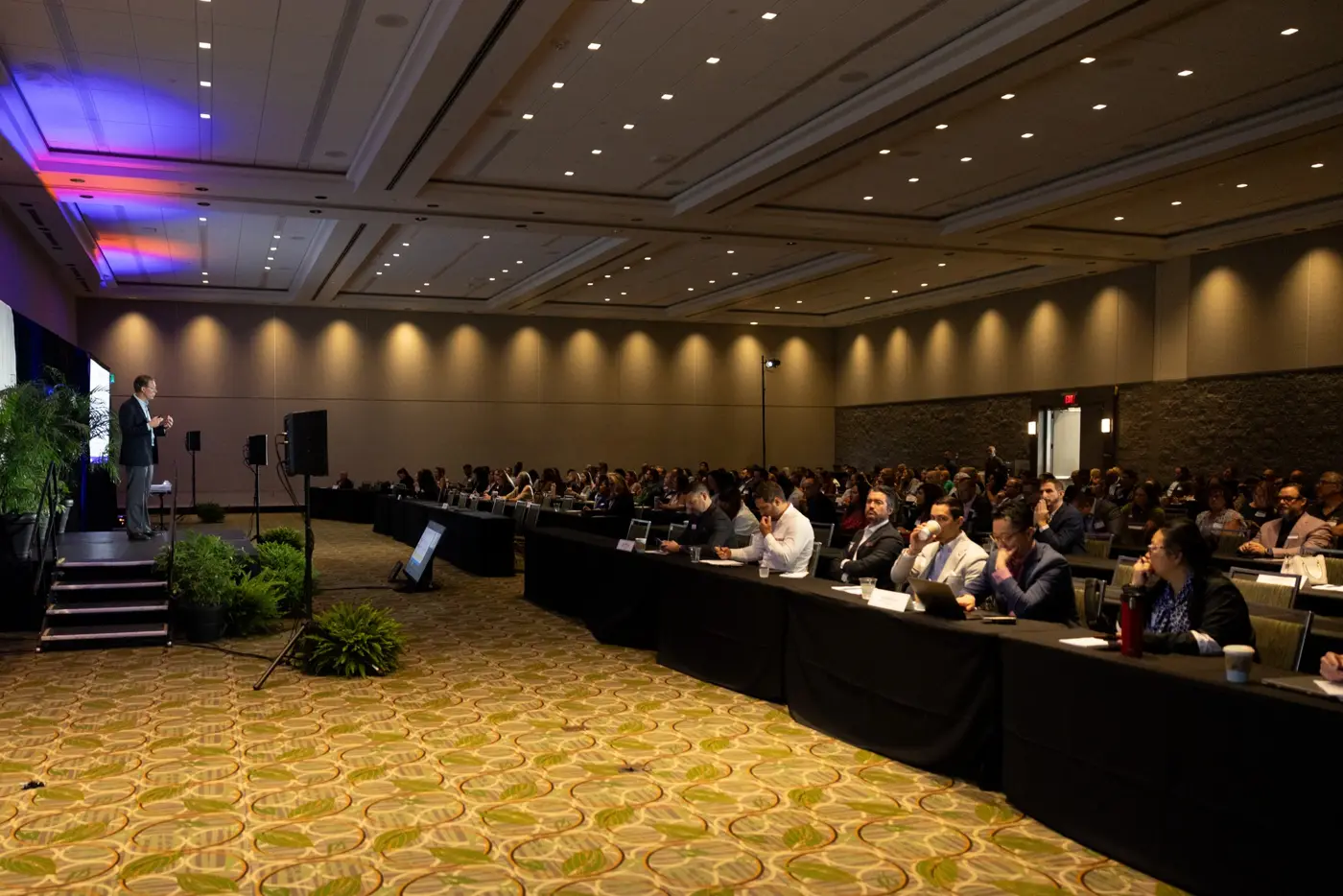 Attendees sit facing a speaker in a conference room.