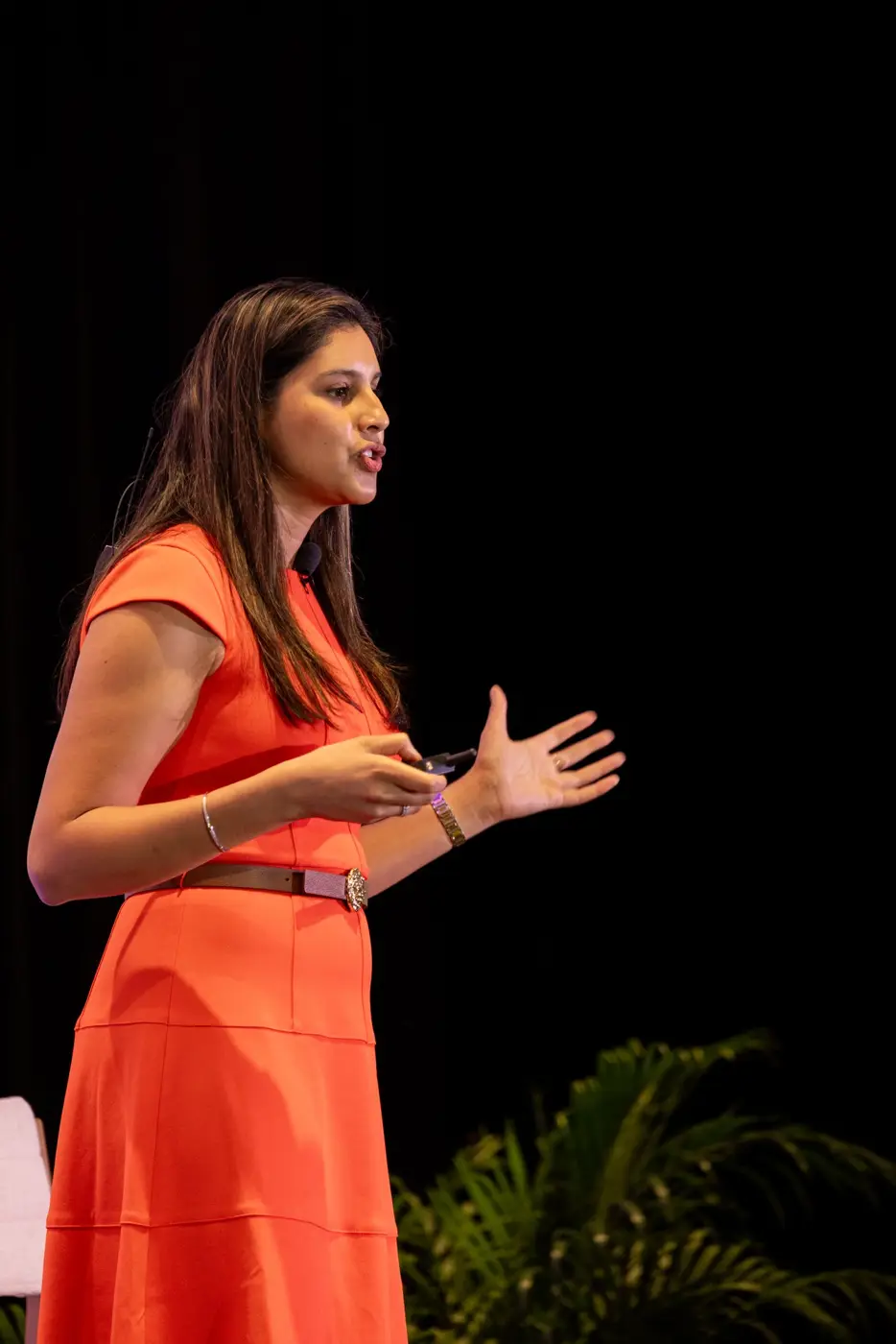 A speaker in an orange dress gestures toward the audience.
