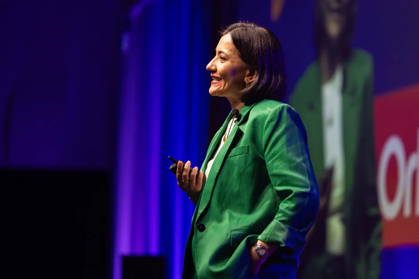 A speaker in a green suit smiles while speaking onstage.