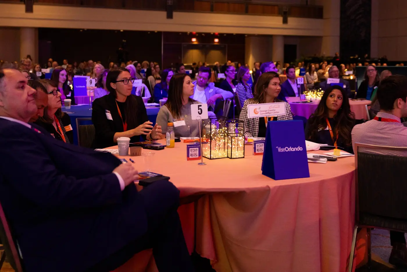 Guests sit at a round table under colorful event lighting.